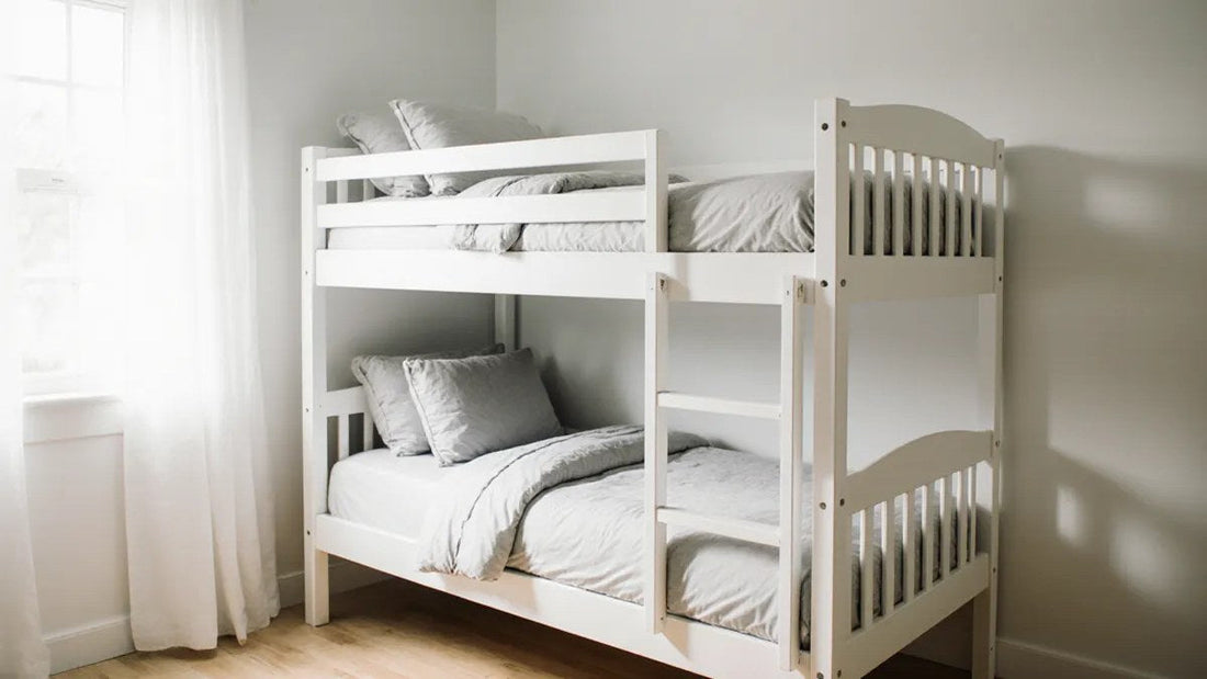 White wooden twin-over-twin bunk bed with guardrail and low-profile mattresses in a sunlit bedroom