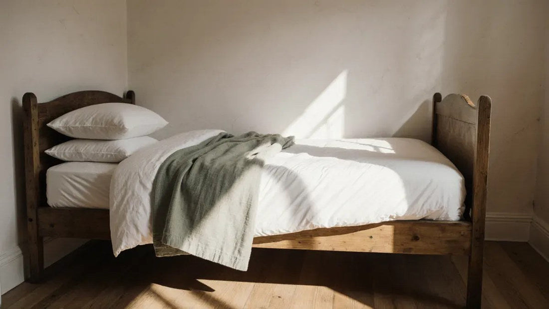 A narrow vintage wooden bed frame made up with white bedding in a sunlit bedroom, similar in width to a three quarter bed